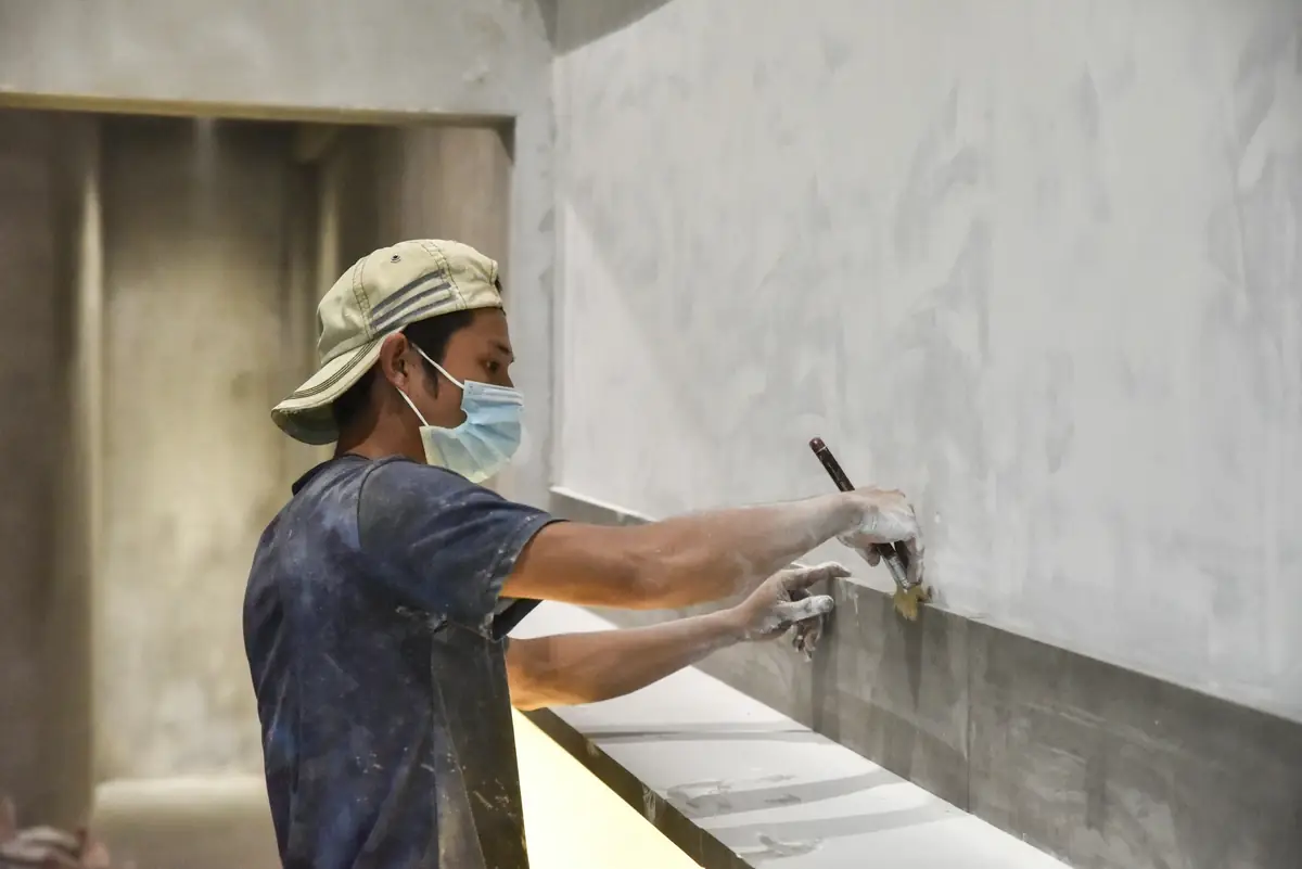 Artisan qui étale la colle à la spatule le long d’un mur, avant la pose