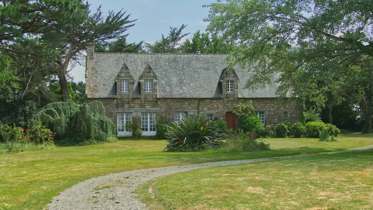 Maison en pierre de granit sous un toit d’ardoise, entourée de pelouse et d’arbres