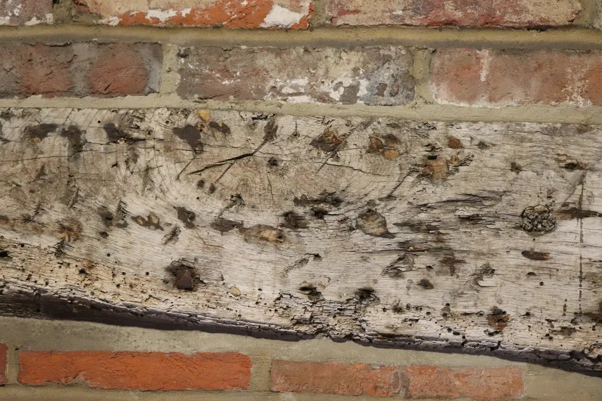Poutre de bois usée et fendillée, prise dans un mur de briques