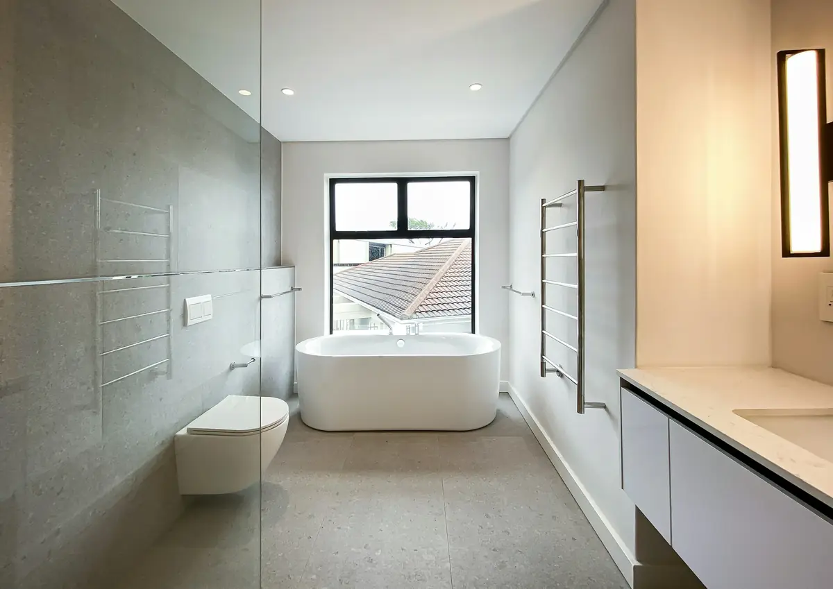 Salle de bain en grands carreaux gris clair, baignoire îlot sous la fenêtre