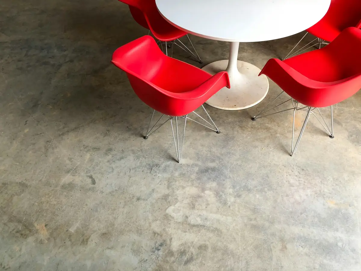 Sol en béton lissé aux reflets nuancés, chaises rouges autour d’une table blanche